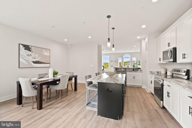 kitchen featuring white cabinets, a kitchen island, stainless steel appliances, light hardwood / wood-style flooring, and decorative light fixtures