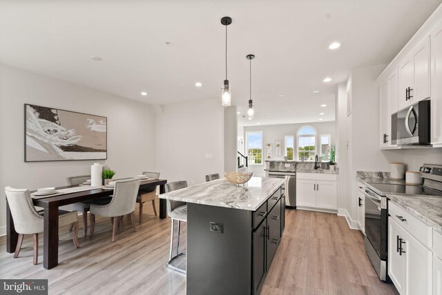 kitchen with light wood-type flooring, a center island, white cabinets, appliances with stainless steel finishes, and decorative light fixtures