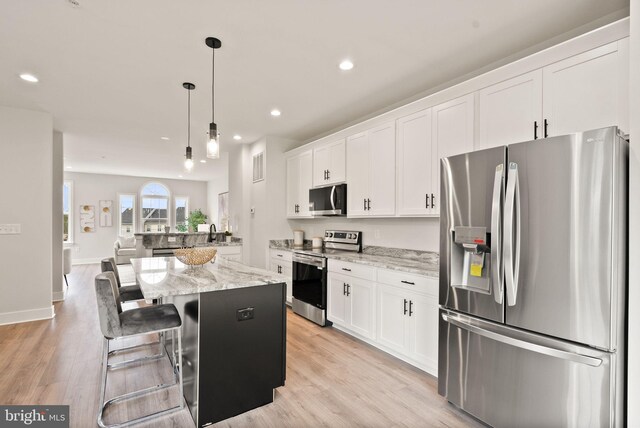 kitchen with light hardwood / wood-style floors, white cabinetry, appliances with stainless steel finishes, a center island, and a kitchen bar