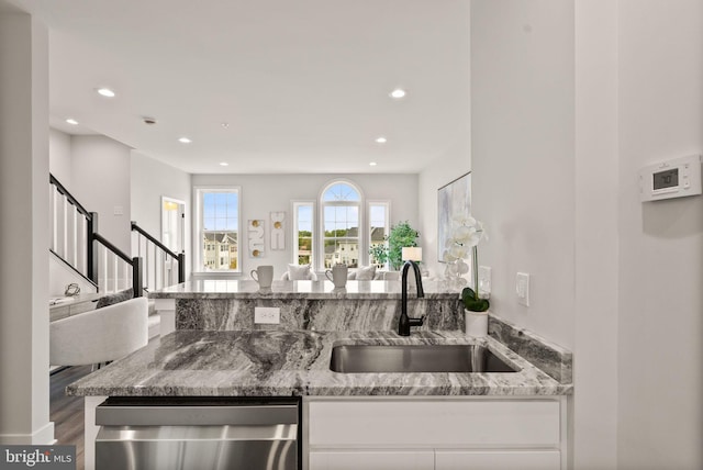 kitchen with white cabinets, sink, dishwasher, light stone countertops, and hardwood / wood-style floors