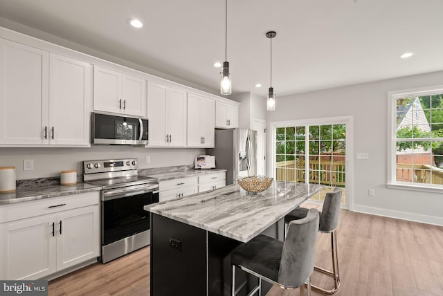 kitchen with white cabinets, hanging light fixtures, a kitchen island, light hardwood / wood-style flooring, and stainless steel appliances