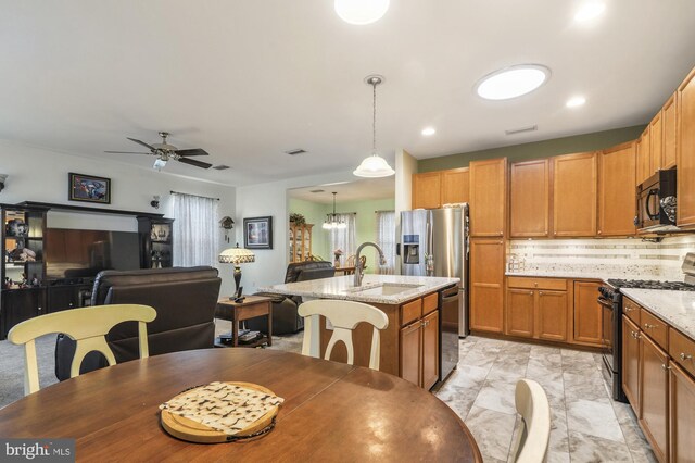 kitchen featuring hanging light fixtures, decorative backsplash, light stone countertops, black appliances, and a kitchen island with sink