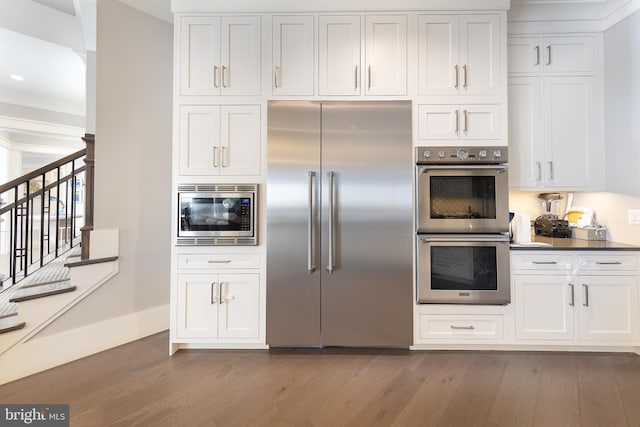 kitchen featuring built in appliances, white cabinetry, dark hardwood / wood-style flooring, and crown molding