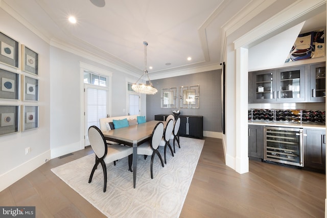 dining area with bar area, light hardwood / wood-style floors, beverage cooler, and ornamental molding