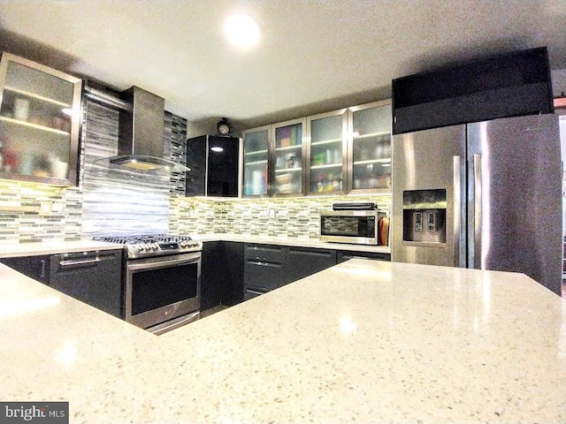 kitchen with appliances with stainless steel finishes, backsplash, light stone countertops, and wall chimney range hood