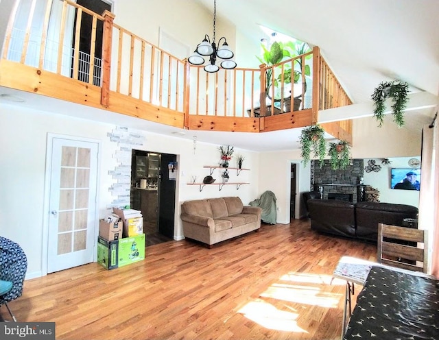 living room featuring a stone fireplace, a high ceiling, an inviting chandelier, and hardwood / wood-style floors