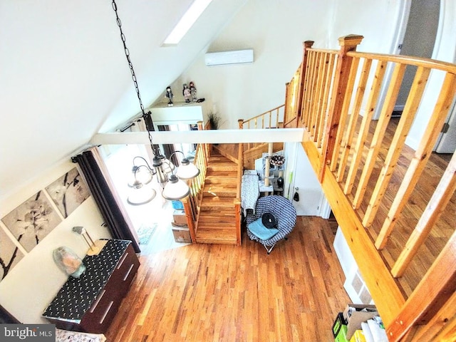 stairs featuring an AC wall unit, hardwood / wood-style floors, and lofted ceiling with skylight