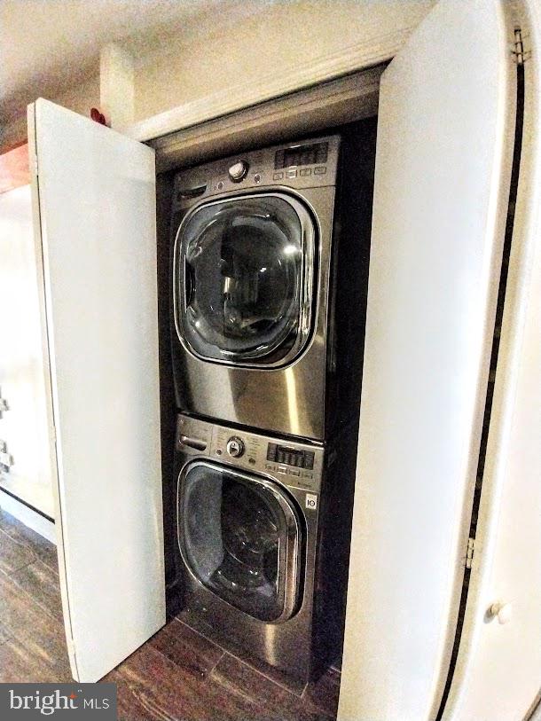 laundry room with dark wood-type flooring and stacked washer and dryer