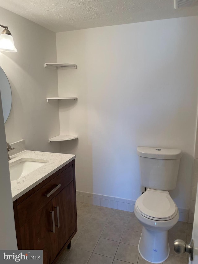 bathroom featuring tile patterned flooring, vanity, a textured ceiling, and toilet