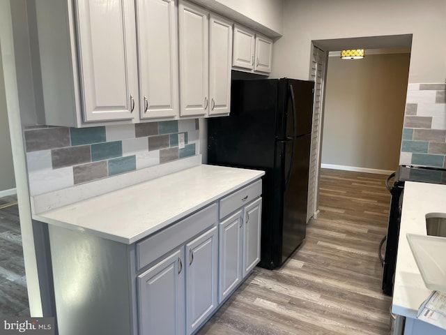 kitchen with tasteful backsplash, white cabinetry, black fridge, and light hardwood / wood-style floors