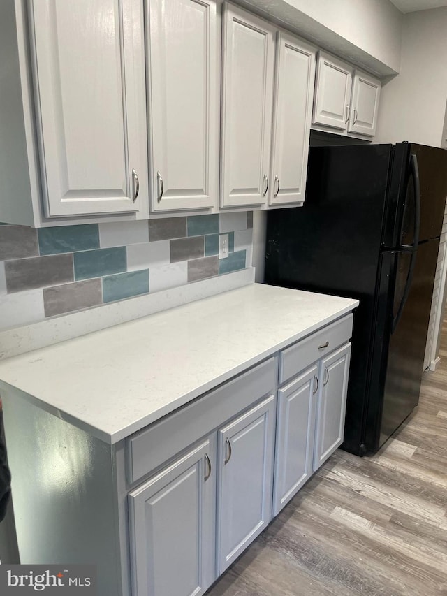 kitchen with black refrigerator, white cabinetry, light hardwood / wood-style floors, and tasteful backsplash