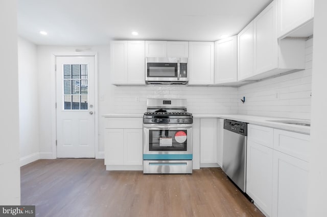 kitchen featuring wood finished floors, stainless steel appliances, decorative backsplash, light countertops, and white cabinets