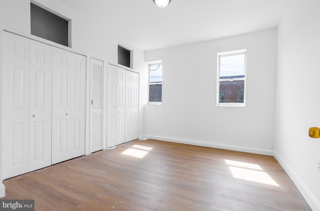 unfurnished bedroom featuring baseboards, multiple closets, and wood finished floors