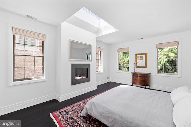 bedroom featuring visible vents, baseboards, a skylight, a glass covered fireplace, and dark wood-style flooring