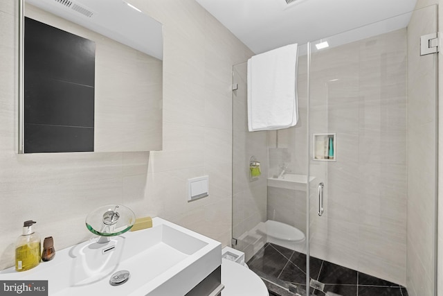 bathroom featuring tile walls, toilet, visible vents, and a stall shower