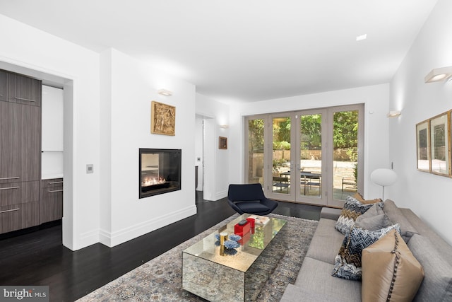 living room featuring a glass covered fireplace, dark wood-style floors, and baseboards