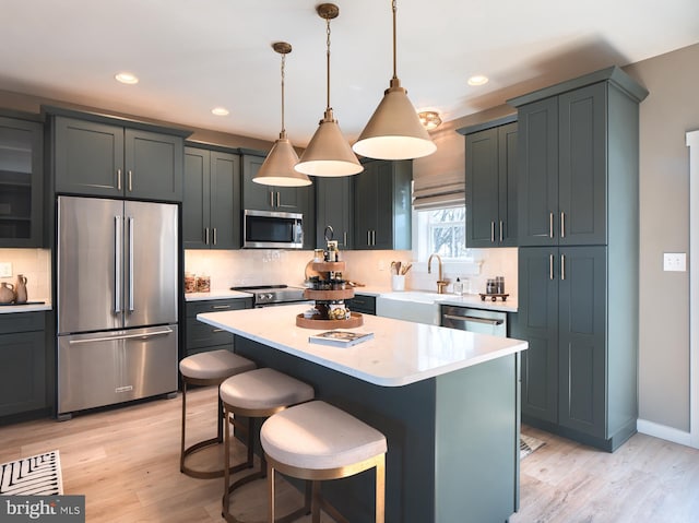 kitchen with a kitchen island, light wood-type flooring, stainless steel appliances, and hanging light fixtures