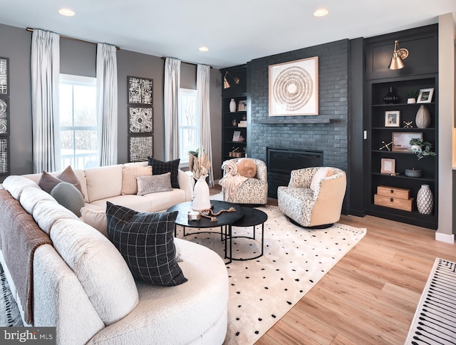 living room with built in shelves, a fireplace, and light wood-type flooring