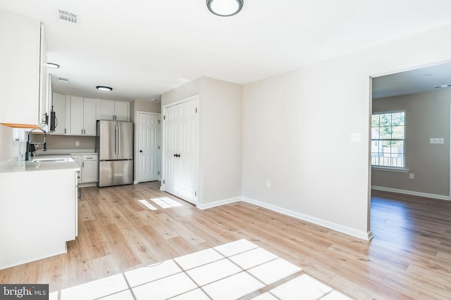 kitchen featuring stainless steel refrigerator, light wood-type flooring, sink, and white cabinetry