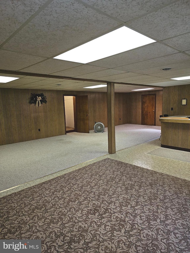 basement featuring a drop ceiling, wooden walls, carpet, and indoor bar