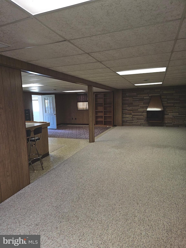 basement with carpet, a drop ceiling, and wooden walls