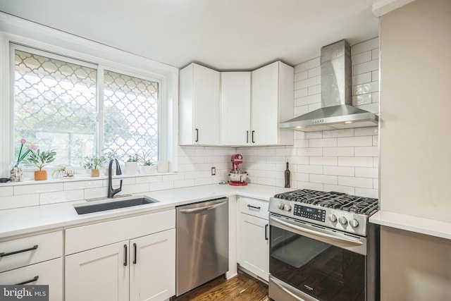 kitchen featuring wall chimney exhaust hood, white cabinets, appliances with stainless steel finishes, and sink