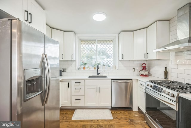 kitchen featuring sink, white cabinets, wall chimney range hood, appliances with stainless steel finishes, and dark hardwood / wood-style flooring