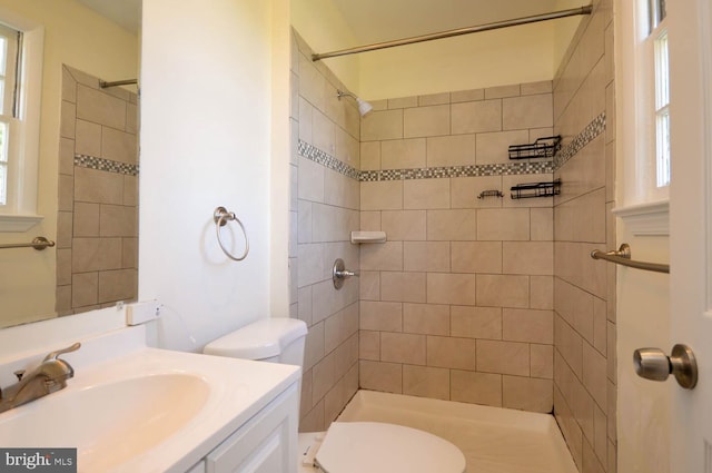 bathroom with a wealth of natural light, vanity, toilet, and tiled shower