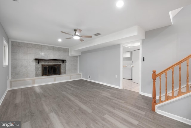 unfurnished living room with tile walls, washer / clothes dryer, a tile fireplace, light wood-type flooring, and ceiling fan