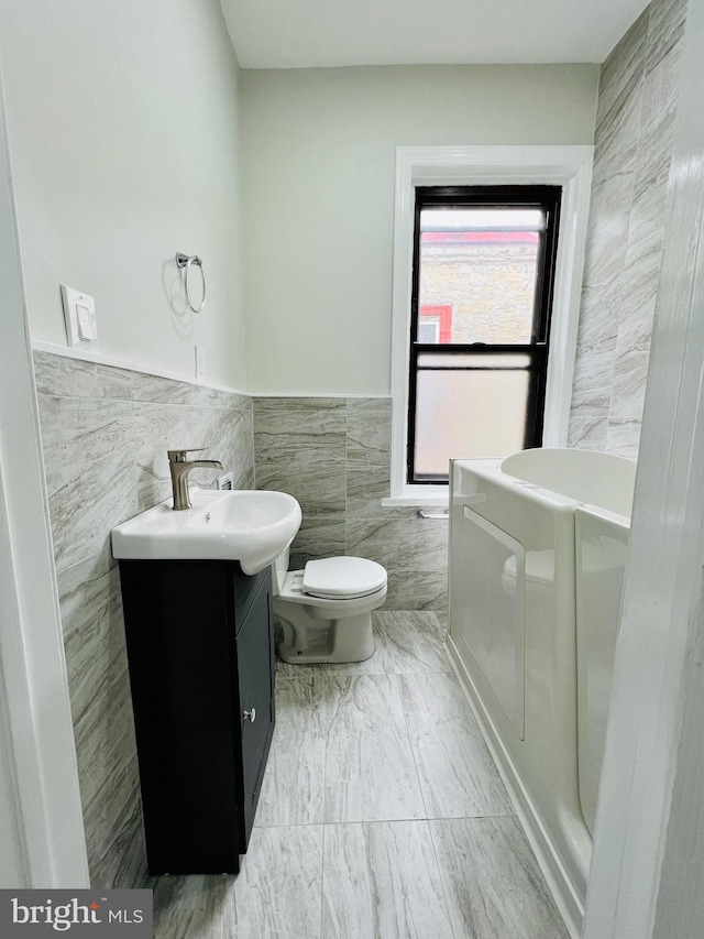 bathroom with vanity, toilet, tile walls, and a washtub