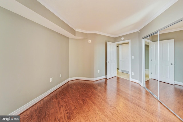 unfurnished bedroom with wood-type flooring, a closet, and crown molding