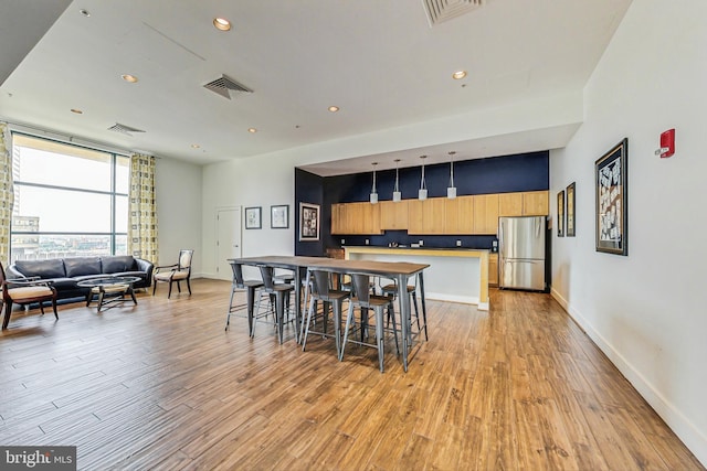 kitchen with a kitchen breakfast bar, stainless steel fridge, light hardwood / wood-style flooring, and hanging light fixtures