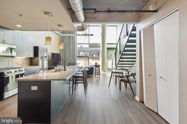 kitchen featuring light wood-type flooring, white cabinetry, stainless steel appliances, a center island with sink, and decorative light fixtures