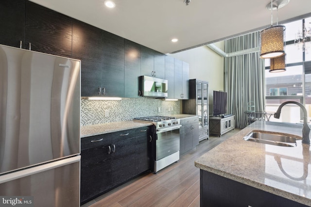 kitchen with light wood-type flooring, sink, hanging light fixtures, stainless steel appliances, and backsplash