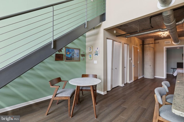 dining space with a towering ceiling and dark wood-type flooring