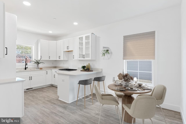 kitchen featuring sink, a kitchen bar, kitchen peninsula, white cabinets, and light hardwood / wood-style flooring