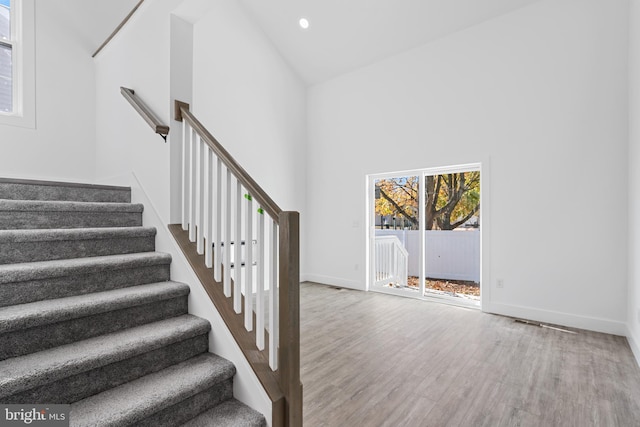 stairway featuring high vaulted ceiling and wood-type flooring