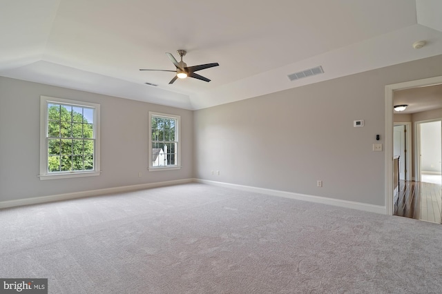 empty room featuring ceiling fan, light colored carpet, lofted ceiling, and a tray ceiling