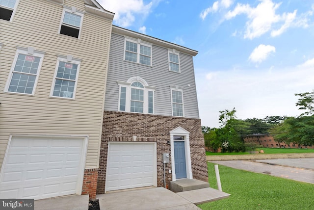 townhome / multi-family property with a front lawn, brick siding, an attached garage, and driveway