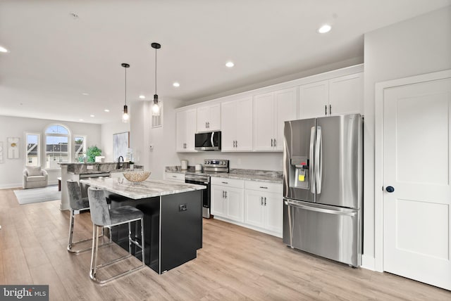 kitchen with appliances with stainless steel finishes, a kitchen island, light hardwood / wood-style flooring, and white cabinets