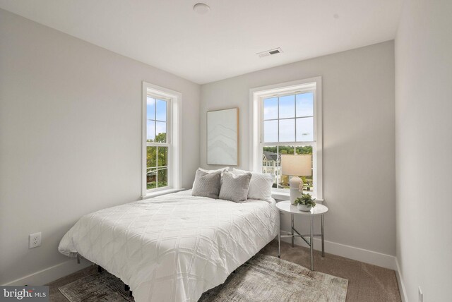 carpeted bedroom with visible vents, multiple windows, and baseboards