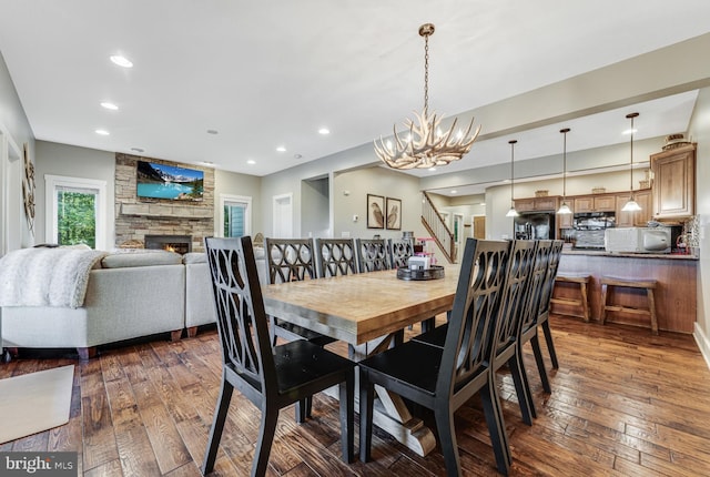 dining space with dark wood-type flooring, a notable chandelier, and a stone fireplace