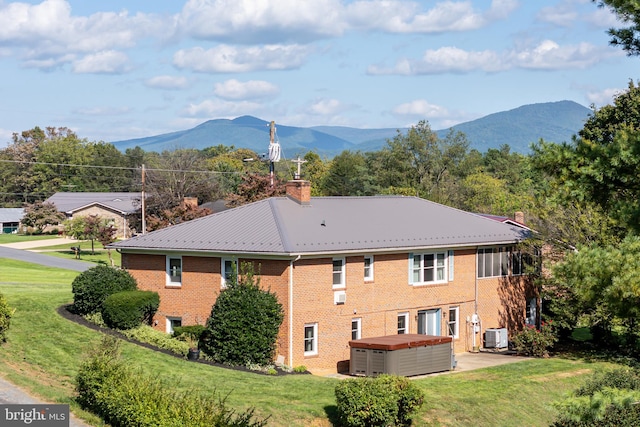 rear view of house featuring a lawn, a hot tub, and a mountain view