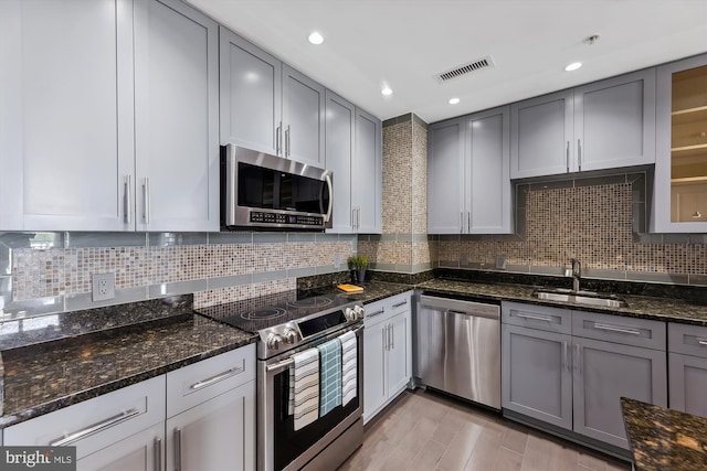 kitchen with appliances with stainless steel finishes, decorative backsplash, dark stone countertops, and sink