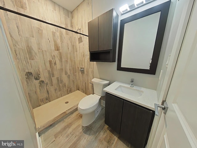 bathroom featuring vanity, a tile shower, hardwood / wood-style flooring, and toilet