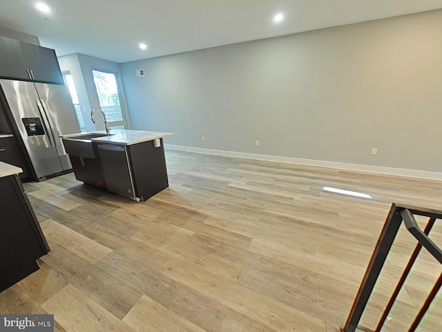 kitchen with sink, stainless steel fridge, a kitchen island with sink, and light wood-type flooring