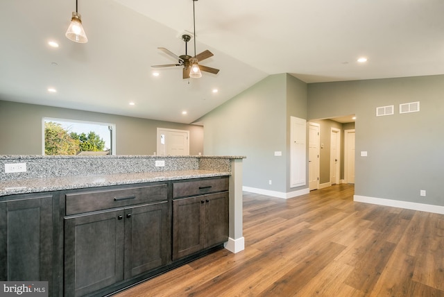 kitchen featuring pendant lighting, lofted ceiling, ceiling fan, light stone countertops, and dark brown cabinetry