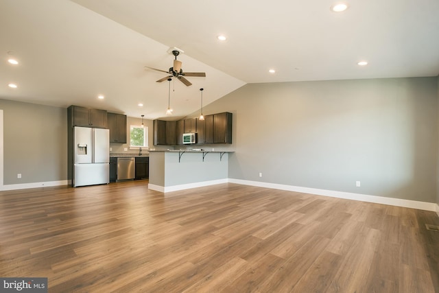 kitchen with appliances with stainless steel finishes, dark brown cabinets, vaulted ceiling, light hardwood / wood-style floors, and a breakfast bar area