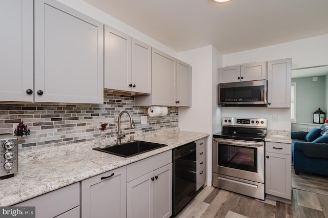 kitchen with light stone countertops, appliances with stainless steel finishes, backsplash, sink, and light hardwood / wood-style flooring