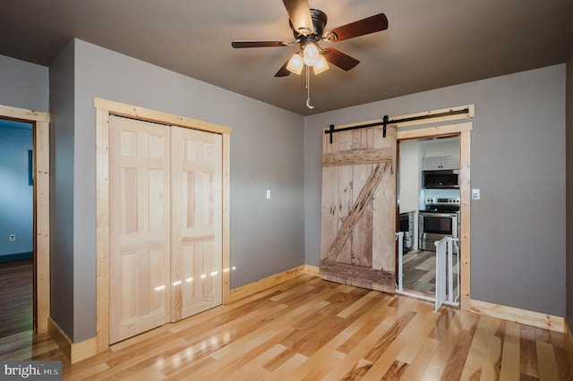 unfurnished bedroom with a barn door, ceiling fan, a closet, and wood-type flooring